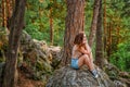 A young woman is sitting on the edge of a cliff overlooking a grand panorama of a pristine forest with rocks Royalty Free Stock Photo