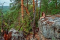 A young woman is sitting on the edge of a cliff overlooking a grand panorama of a pristine forest with rocks Royalty Free Stock Photo