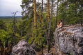 A young woman is sitting on the edge of a cliff overlooking a grand panorama of a pristine forest with rocks Royalty Free Stock Photo