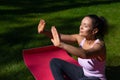 Young woman sitting on a fitness mat on a green grass in the park enjoying sunny day while performing yoga Royalty Free Stock Photo