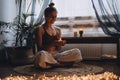 Young woman sitting on the floor, lights candles, enjoy meditation, do yoga exercise at home. Mental health, self care