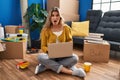 Young woman sitting on the floor at new home using laptop afraid and shocked with surprise expression, fear and excited face Royalty Free Stock Photo