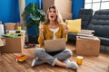Young woman sitting on the floor at new home using laptop amazed and surprised looking up and pointing with fingers and raised Royalty Free Stock Photo
