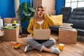 Young woman sitting on the floor at new home using laptop doing ok gesture shocked with surprised face, eye looking through Royalty Free Stock Photo