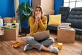 Young woman sitting on the floor at new home using laptop shocked covering mouth with hands for mistake Royalty Free Stock Photo