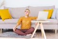 Young woman is sitting on floor by sofa, using laptop. Caucasian woman working Royalty Free Stock Photo