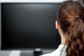 Young woman sitting in front of a black monitor or tv, backview Royalty Free Stock Photo