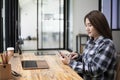 Young woman sitting in front of laptop at office desk and using mobile phone. Royalty Free Stock Photo