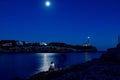 Young woman sitting in front of ocean with moonlight reflection and lighthouse at night. poetic and relaxing image, mindfulness, Royalty Free Stock Photo