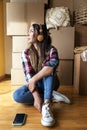 Young woman sitting in front of pile of cardboard boxes wearing headphones. Pensive female looking out the window Royalty Free Stock Photo