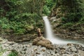 Young woman sitting in front of a waterfall in the middle of a jungle. Wild nature landscape. Long exposure. Flowing water. Green Royalty Free Stock Photo