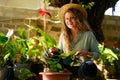 Young woman sitting in garden planting flowers in pots smiles and looks at camera. Junior female gardener with gardening Royalty Free Stock Photo