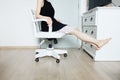Young Woman Sitting. Girl in Black Dress Sit. Beautiful Female Slim Legs on White Chair with Barefeet in the White Room at Condo Royalty Free Stock Photo