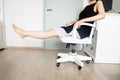 Young Woman Sitting. Girl in Black Dress Sit. Beautiful Female Slim Legs on White Chair with Barefeet in the White Room at Condo Royalty Free Stock Photo