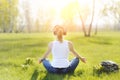 Young woman sitting on grass in Park and meditating and listening to music on headphones.