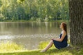 Young woman sitting on grass under high big oak,trunk tree near lake,river,meditating,relaxing in National Park.Teen girl, Royalty Free Stock Photo