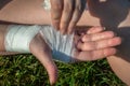 A young woman sitting on green grass outdoors is independently bandaging her injured wrist with a medical gauze bandage. Close-up