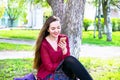 Young woman sitting on a green lawn and holding a cell phone