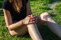 A young woman sitting on a green lawn holds on to a damaged knee. Sprain or cramp Overtrained injured person when training