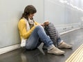 Young woman sitting on ground using phone while leaning on underground platform wall