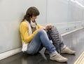 Young woman sitting on ground using phone while leaning on underground platform wall