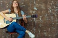 Young woman sitting with guitar on grunge wall background. Royalty Free Stock Photo