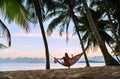 Young woman sitting in hammock swinging on the exotic island sand beach at sunrise time