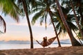 Young woman sitting in hammock swinging on the exotic island sand beach at sunrise time