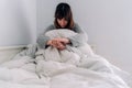 A young woman is sitting on her bed and she is covering herself with a quilt. She has her eyes closed. She is worried and she Royalty Free Stock Photo