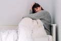 A young woman is sitting on her bed and she is covering herself with a quilt. She has her hand on her head. She is worried and she Royalty Free Stock Photo