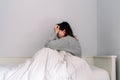 A young woman is sitting on her bed and she is covering herself with a quilt. She has her hands on her eyes. She is worried and Royalty Free Stock Photo