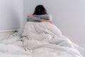 A young woman is sitting on her bed and she is covering herself with a quilt. She has her head on her arms crossbred. She is Royalty Free Stock Photo