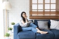 Young woman sitting on her sofa with pillow in hands. Young happy woman at home sitting on modern sofa in front of window relaxing Royalty Free Stock Photo