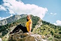 Young woman sitting on hill. Dreamy female sitting on altitude and looking at Peaks of magnificent rocks located against
