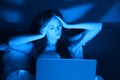 Young woman sitting at home in bed at night with laptop, holds head in her hands