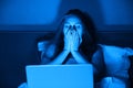 Young woman sitting at home in bed at night with laptop, holds head in her hands