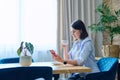 Young woman sitting at home drinking morning coffee, reading news in smartphone Royalty Free Stock Photo