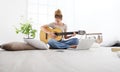Young woman sitting in living room playing guitar at the computer, stay at home concept Royalty Free Stock Photo