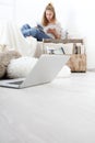 Young woman sitting in living room reading a book with your computer nearby, stay at home concept