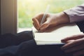 Young woman sitting next to the window writing notes on notebook with pen Royalty Free Stock Photo