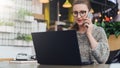 Young woman sitting in office, cafe at table in front of laptop and talking on mobile phone. Freelancer works in a cafe. Royalty Free Stock Photo