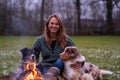 Young woman is sitting outside in the woods with her two Australian Shepherd dogs. Snow on the grass, twilight by the