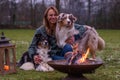 Young woman is sitting outside in the woods with her two Australian Shepherd dogs. Snow on the grass, twilight by the