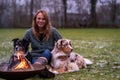 Young woman is sitting outside in the woods with her two Australian Shepherd dogs. Snow on the grass, twilight by the