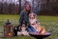 Young woman is sitting outside in the woods with her two Australian Shepherd dogs. Snow on the grass, twilight by the