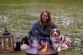 Young woman is sitting outside in the woods with her two Australian Shepherd dogs. Snow on the grass, twilight by the