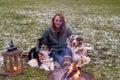 Young woman is sitting outside in the woods with her two Australian Shepherd dogs. Snow on the grass, twilight by the