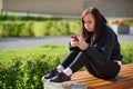 Young woman sitting on a Park bench, looking at her mobile phone. A woman using a smartphone uses the Internet in the Royalty Free Stock Photo