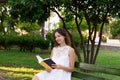 Young woman is sitting in the park and enjoys reading a book