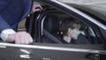 Young woman sitting in passenger compartment of the new car in car showroom. Professioal seller in suit consulting